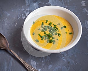 Soup of mashed potatoes with vegetables and cheese sprinkled with green onions, a tablespoon on a gray background