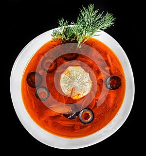 Soup with meat, olives, herbs and lemon in bowl, isolated on black background, homemade food.