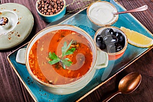 Soup with meat, olives, herbs, lemon, sour cream in bowl, black bread and spices on dark wooden background, homemade food