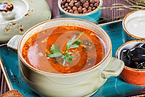 Soup with meat, olives, herbs, lemon, sour cream in bowl, black bread and spices on dark wooden background, homemade food