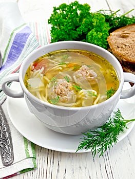 Soup with meatballs and noodles in white bowl on board