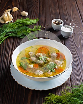 Soup with meatballs in a white plate with sauce and herbs on a wooden table.