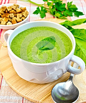 Soup puree with spinach leaves and spoon on fabric