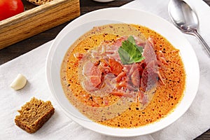 Soup, Russian borscht with sour cream and parsley in a white plate, garlic, spoon, bread, on a white towel on a brown wooden