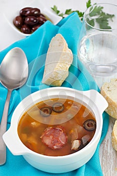 Soup with saisages and olives in the bowl with glass