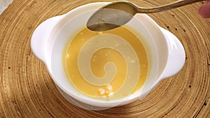 Soup with shrimp in a white plate on a round wooden tray. A woman stirs the soup with a spoon