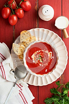 Soup. Tomato cream soup or gazpacho with herbs, seasonings, cherry tomato and parsley in white bowl on old red wooden background.