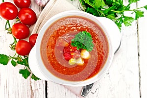 Soup tomato in white bowl with vegetables and parsley on board t
