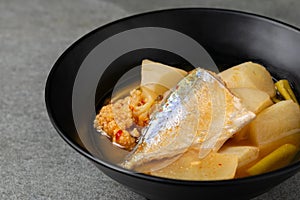 Sour curry with papaya and half fish in black bowl on the concrete table