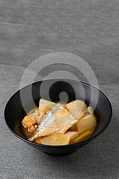 Sour curry with papaya and half fish in black bowl on the concrete table