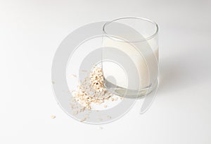 Sour milk in a glass next to raw oatmeal flakes on a white background