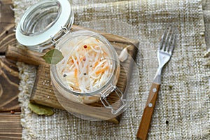 Sour, pickled sauerkraut with carrots and bay leaves in a glass jar