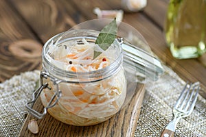 Sour, pickled sauerkraut with carrots and bay leaves in a glass jar