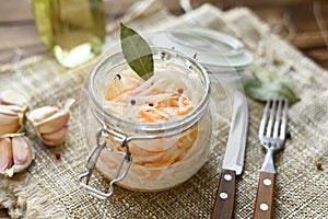 Sour, pickled sauerkraut with carrots and bay leaves in a glass jar