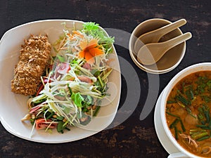Sour and spicy Tom Yum Goong soup and salad with green mango and breaded fish on plate on a table in a restaurant. Thai Authentic