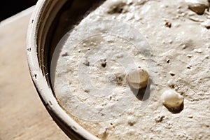 Sourdough bread proofing in a basket with visible gas bubbles. Homemade baking