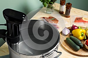 Sous vide cooker in pot and ingredients on table, closeup. Thermal immersion circulator