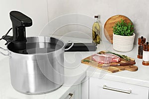 Sous vide cooker in pot and ingredients on white countertop. Thermal immersion circulator