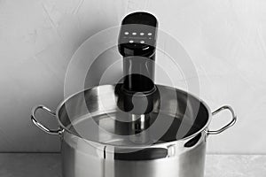 Sous vide cooker in pot on light grey table. Thermal immersion circulator