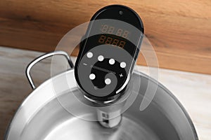 Sous vide cooker in pot on white wooden table, closeup. Thermal immersion circulator