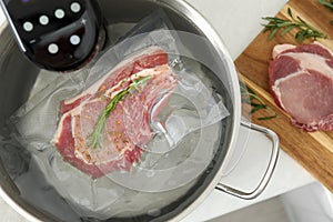 Sous vide cooker and vacuum packed meat in pot on white table, top view. Thermal immersion circulator