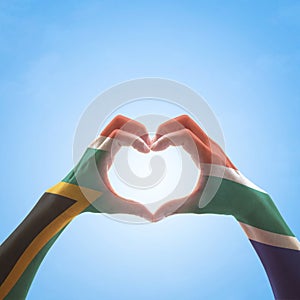 South Africa flag on woman hands in heart shape isolated on blue sky background for national unity, union, love and reconciliation