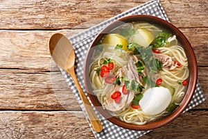 South American Caldo de Gallina chicken noodle soup with boiled egg and herbs close-up in a plate. horizontal top view photo