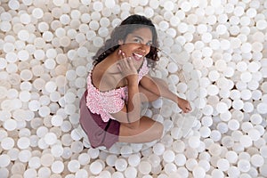 South American girl kneels between plastic balls, she is smiling and happy, advertising photo, concept of femininity and happiness