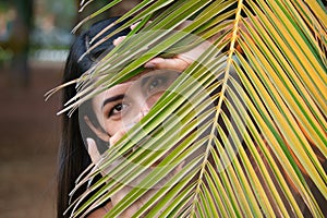 South American woman, young and beautiful, brunette, looking through the leaves of a palm tree. Concept beauty, looks, plants,