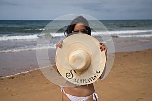 South American woman, young and beautiful, brunette with sunglasses and bikini and covering her face with a hat with the word