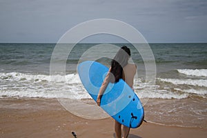 South American woman, young and beautiful, brunette with sunglasses and swimsuit, running into the water holding a blue surfboard