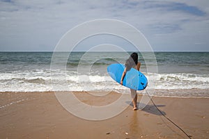 South American woman, young and beautiful, brunette with sunglasses and swimsuit, running into the water holding a blue surfboard