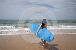 South American woman, young and beautiful, brunette with sunglasses and swimsuit, running into the water holding a blue surfboard