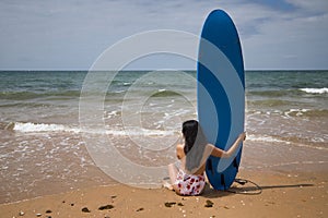 South American woman, young and beautiful, brunette with sunglasses and swimsuit, sitting on her back and holding a blue surfboard