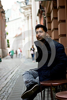 A south asian Indian ethnicity man sitting in an open street side restaurant located in central europe. Low angle shot of a
