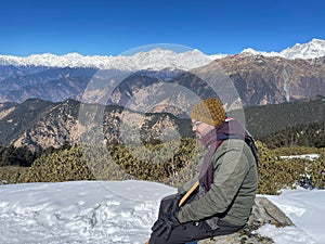 South Asian man sitting atop a snow-covered hill in Chandrashila trek, Uttarakhand