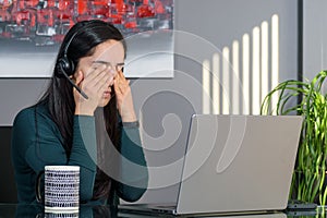 South Asian woman having a stressful business call in headphones at a desk in home office