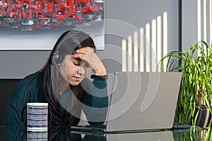 South Asian woman having a stressful business call in headphones at a desk in home office