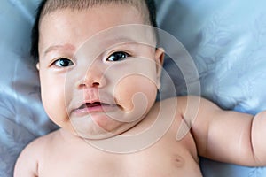 South East Asian new born isnâ€™t wearing shirt. Newborn face is upset. Baby is laying on the bed. Infant is 4 months old.