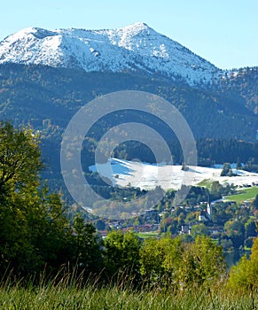 South German landscape with a village in the valley, mountain forest and majestic mountain with snow in the background