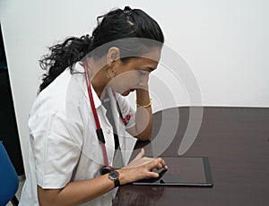 A south Indian female doctor in 30s browsing tablet in white coat and red stethoscope in white background