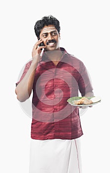South Indian man holding a plate of food and talking on a mobile