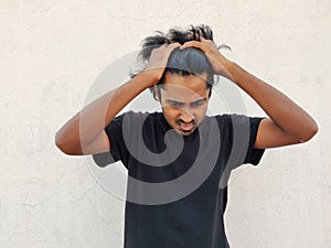 black tshirt rending his hair, looking down and feeling sad ,holding hands on head. White photo