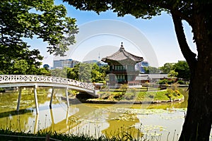 South Korea, Seoul. Gyeongbokgung palace area garden and park. Hyangwonjeong pavilion and bridge. City skyline in the background.