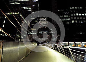 The South Quay Footbridge To The Brightly Lit Bank Towers Of Canary Wharf  London England At Night