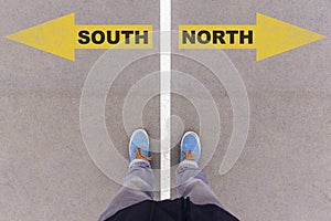 South vs North text arrows on asphalt ground, feet and shoes on