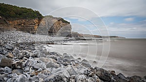 South Wales coastline, showing the water lapping against the rocky shore, flanked by high cliff.