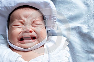 Southeast Asian baby colic is wearing white hat and shirt. South East Asian newborn is crying. Newborn is unhealthy.