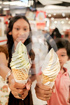 Southeast Asian children, boy and teen girl showing green tea and vanilla ice cream cones at food court