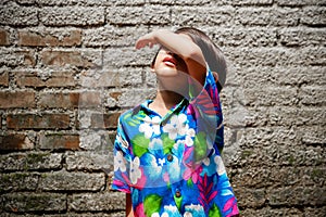 Southeast Asian ethnicity little boy sunbathing in the morning at the backyard at home. hand raising up to cover her face